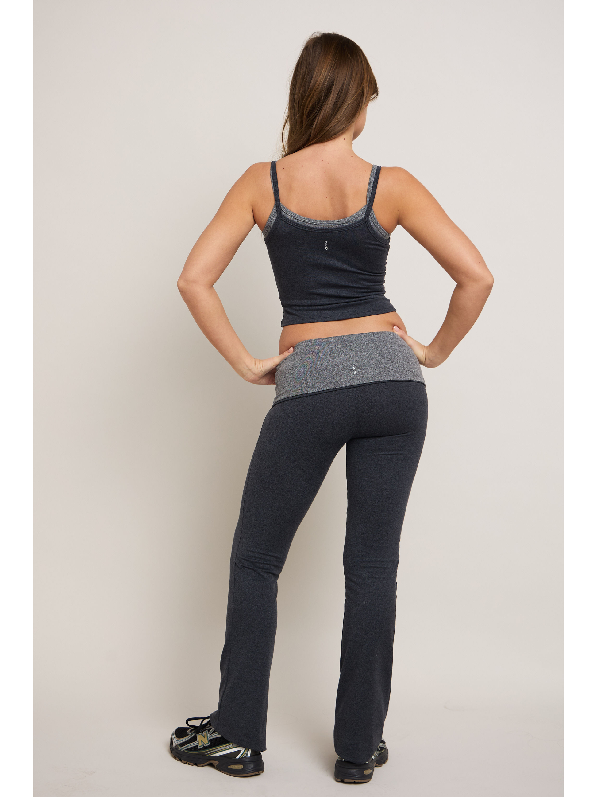 Woman wearing a tank top and gray leggings on a plain background