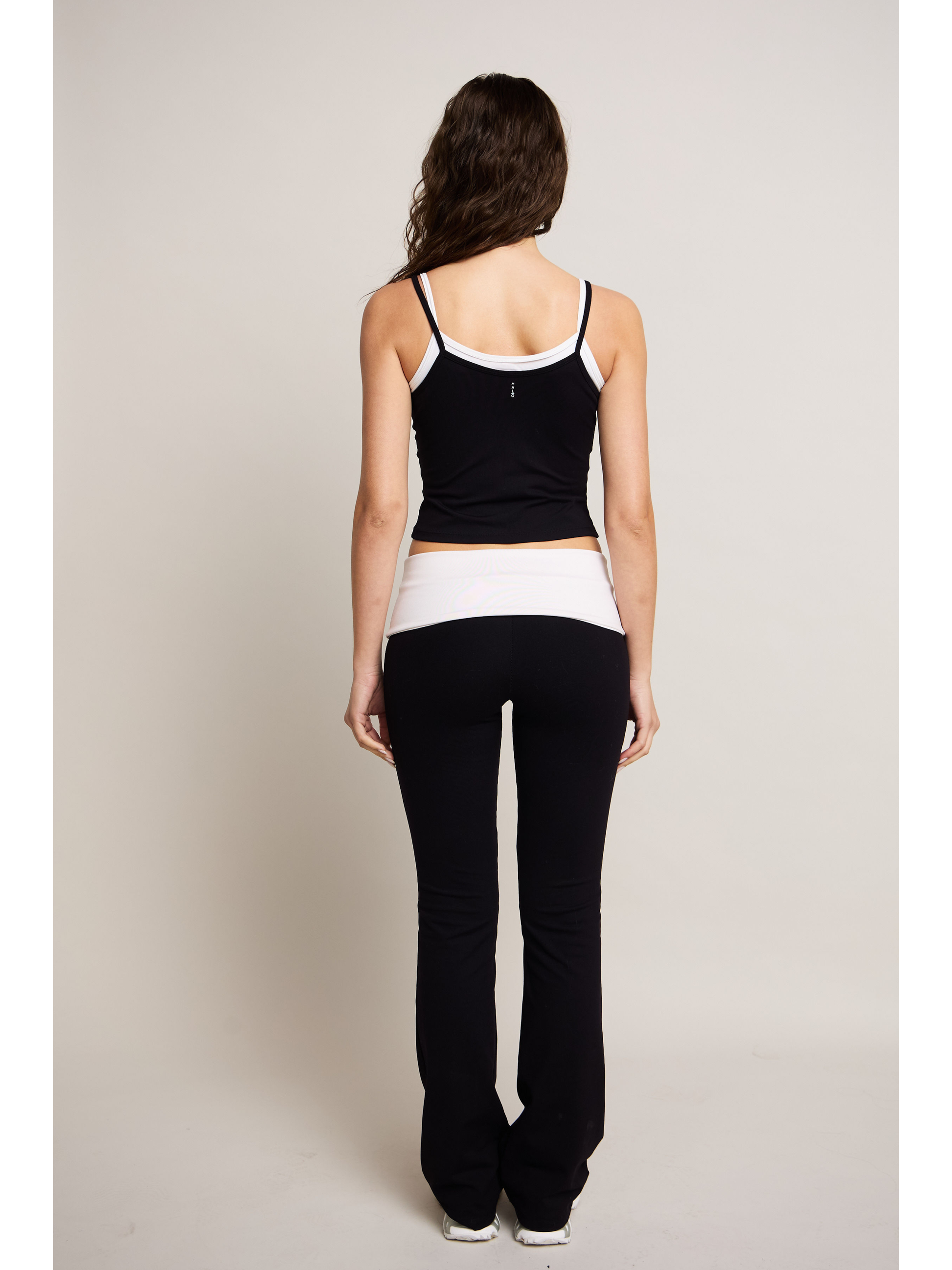 Woman wearing a black and white tank top and black pants on a plain background