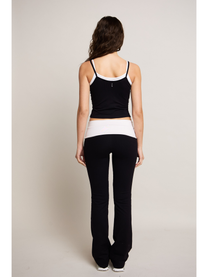 Woman wearing a black and white tank top and black pants on a plain background