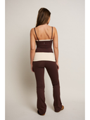 Woman wearing a two-tone top and brown pants on a plain background