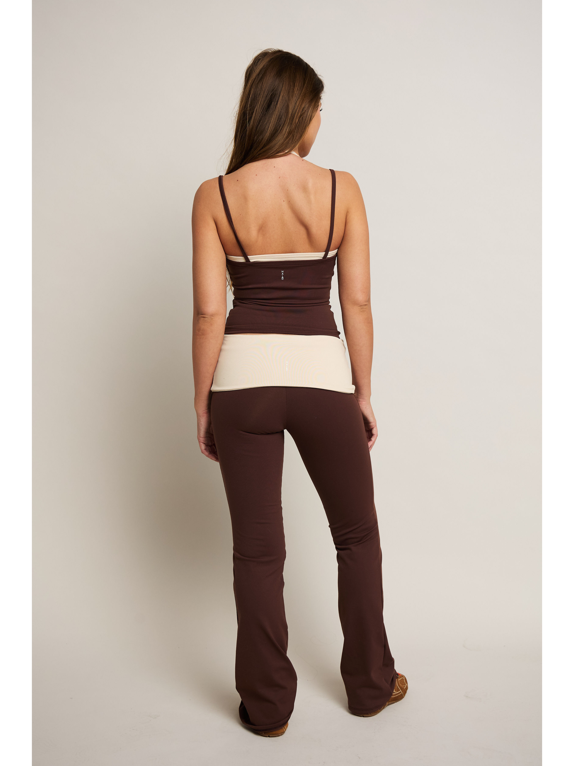 Woman wearing a two-tone top and brown pants on a plain background