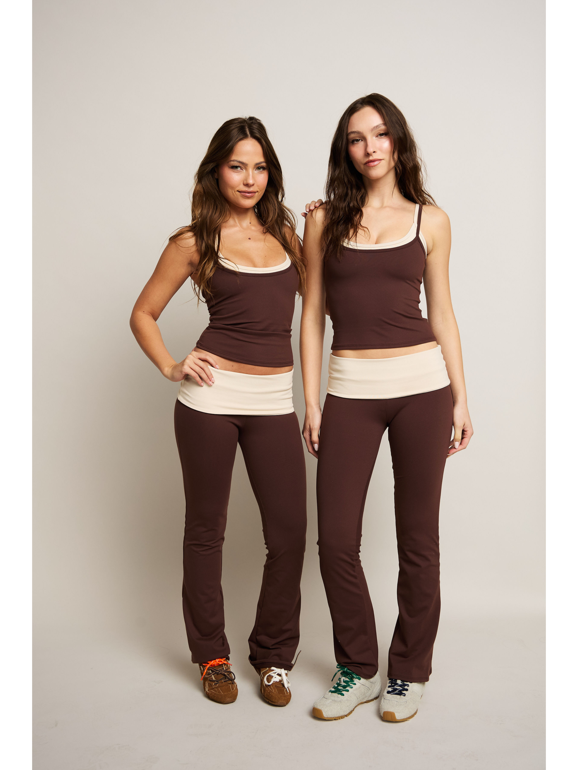 Two women wearing matching brown and beige outfits on a plain background