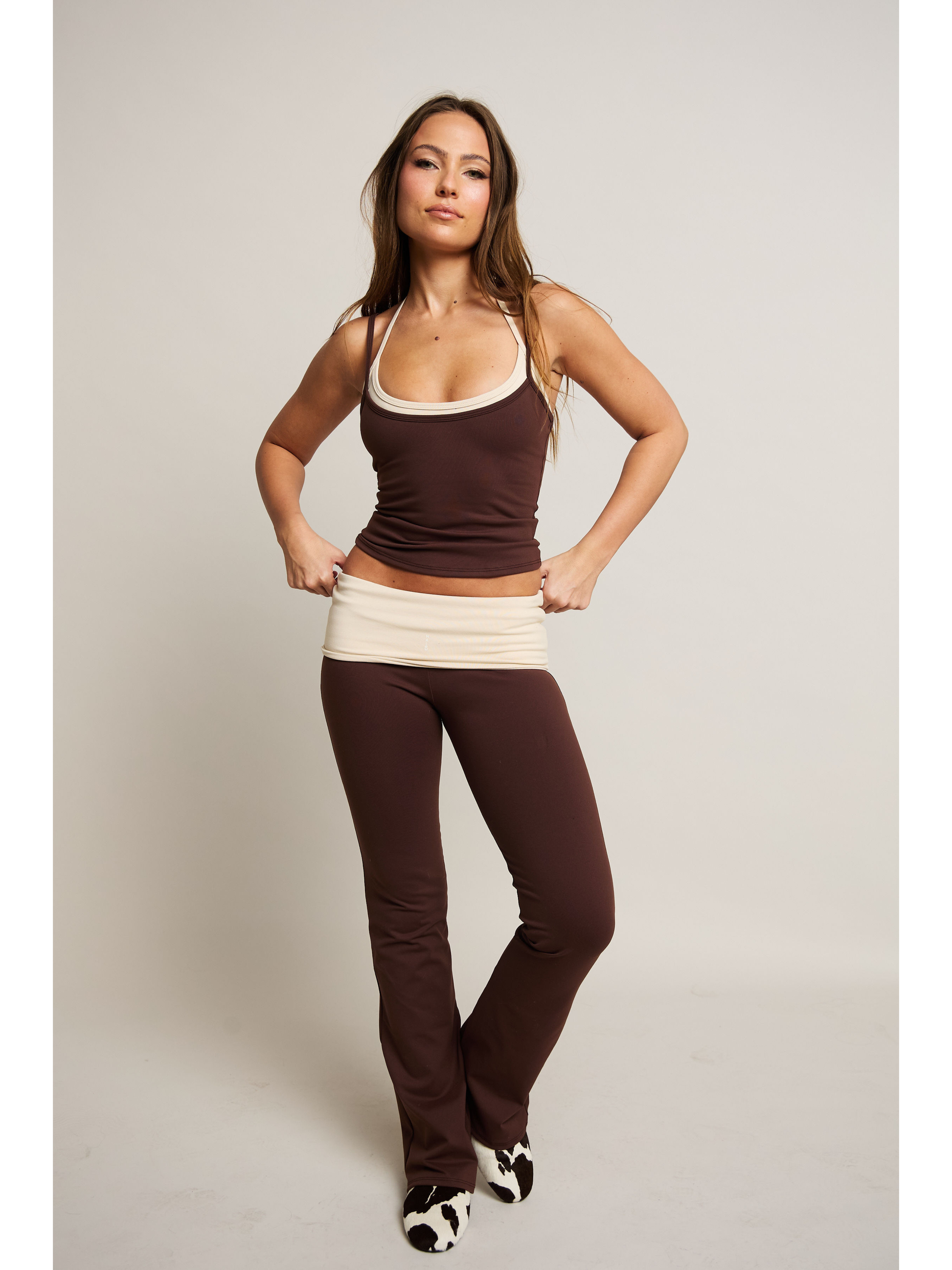 Woman wearing a brown tank top and pants on a plain background